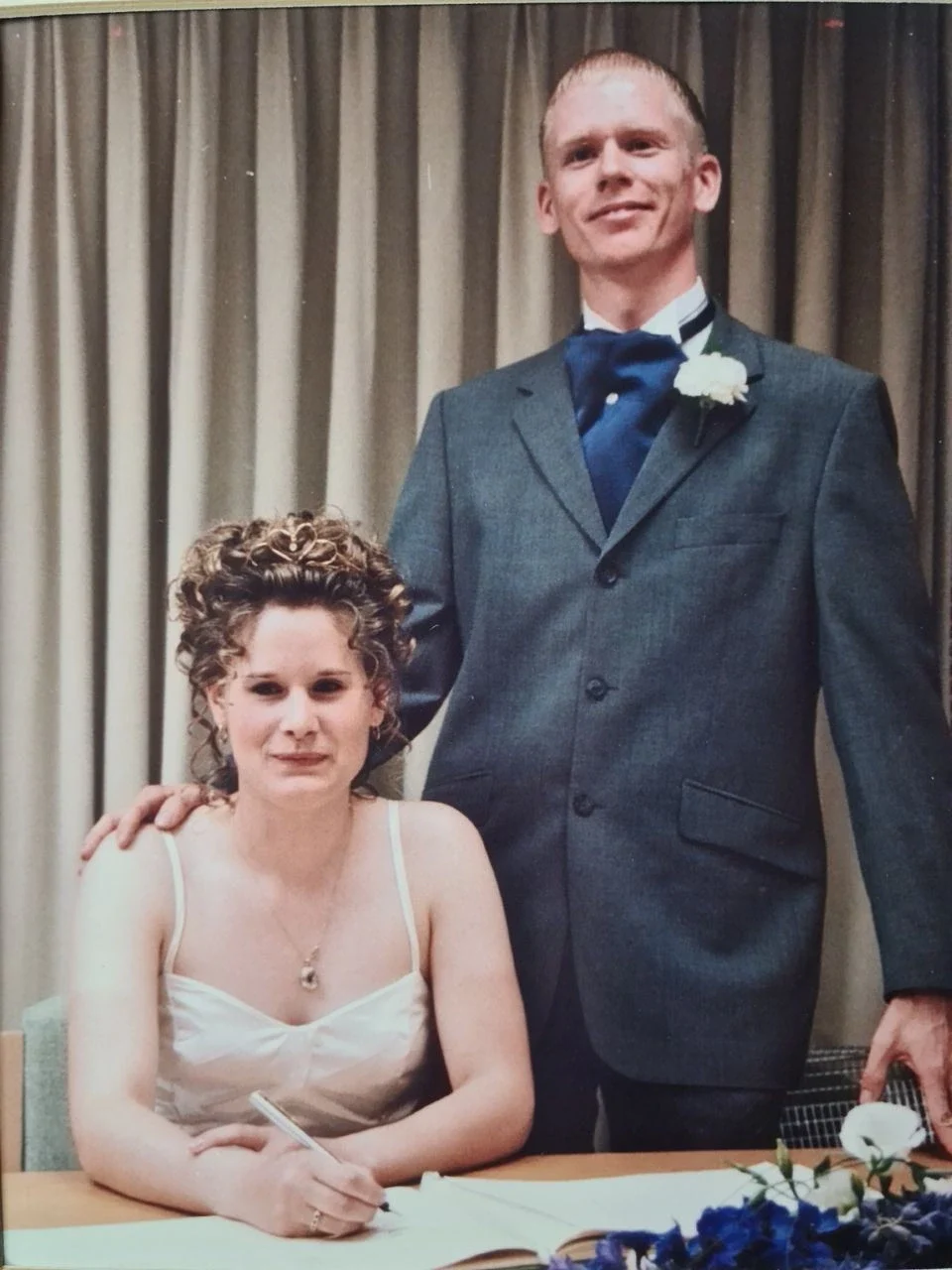 Bride and groom at a wedding, posing at a table with floral decorations.